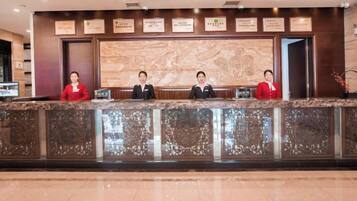 A reception desk with three staff members, a marble wall with plaques, and a polished floor.