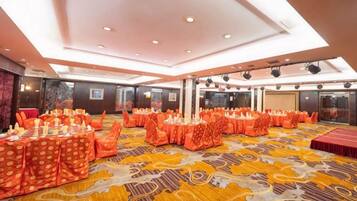 A banquet hall with round tables, chairs, and a patterned carpet.