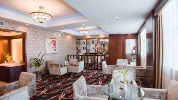 A hotel lobby with a patterned carpet, round tables, and chairs, a reception desk, and a bar area.
