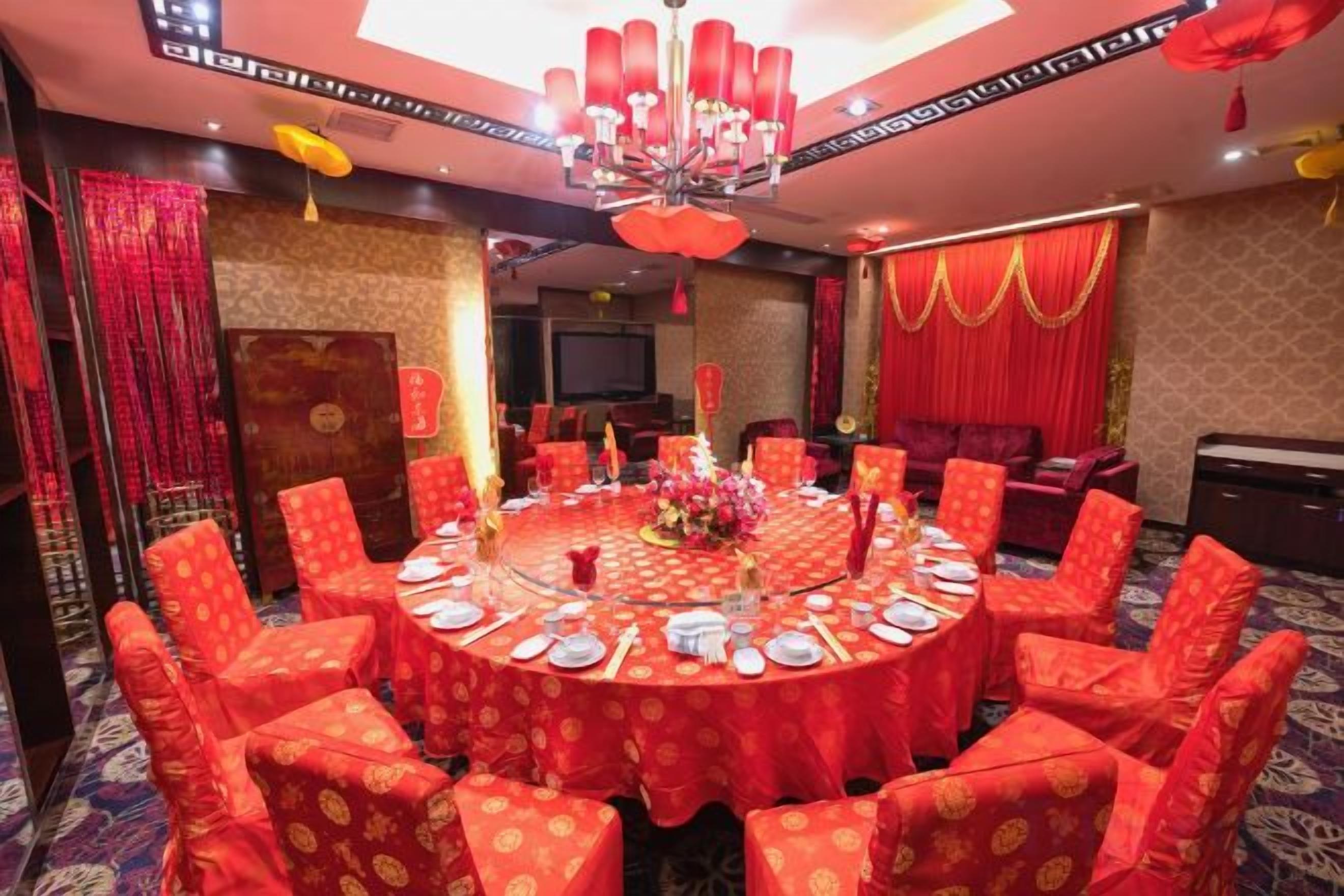 Un salón de banquetes con mesas redondas y sillas rojas, un candelabro y cortinas rojas.