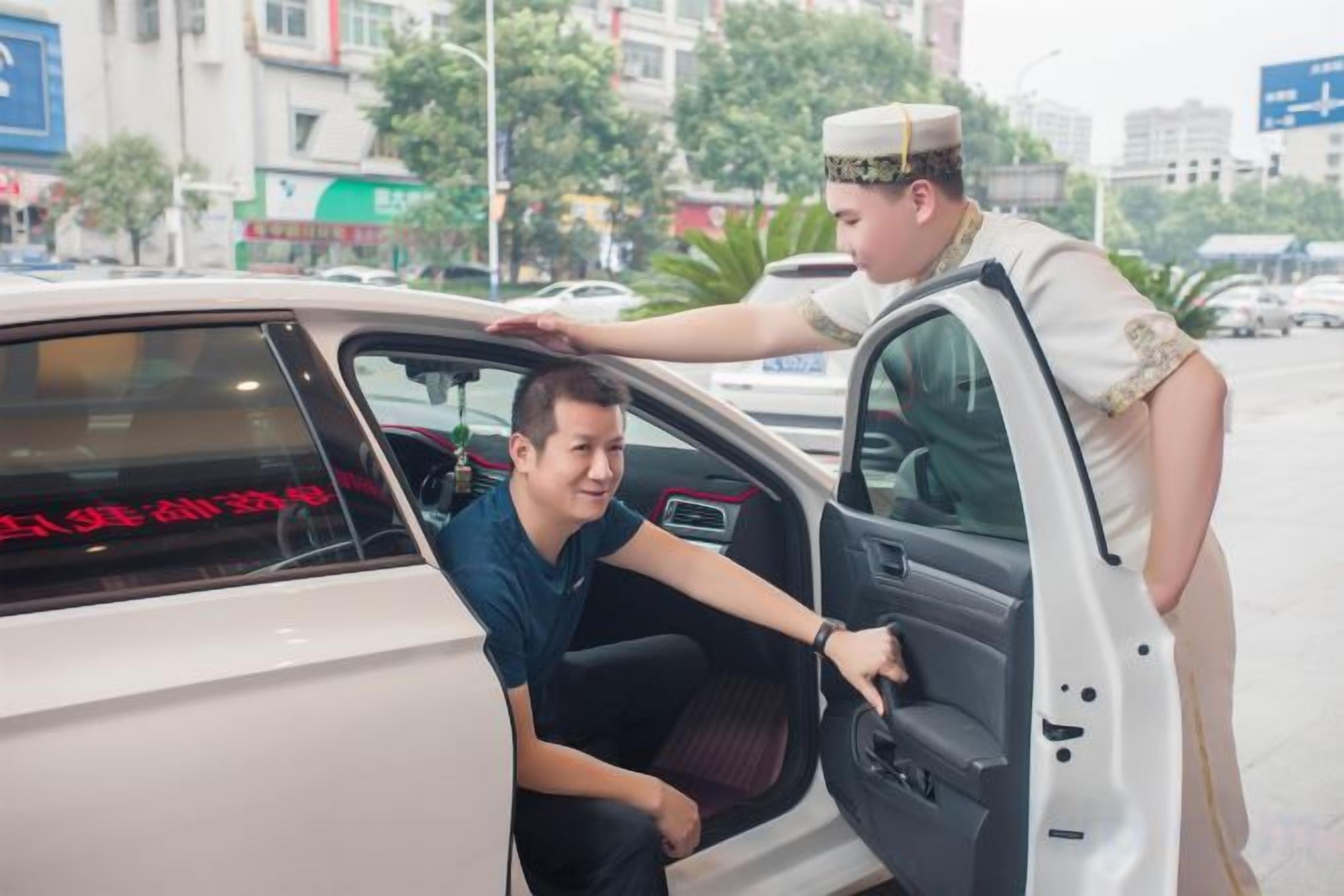 Una persona ayuda a otra a entrar en un coche, con una calle urbana al fondo.