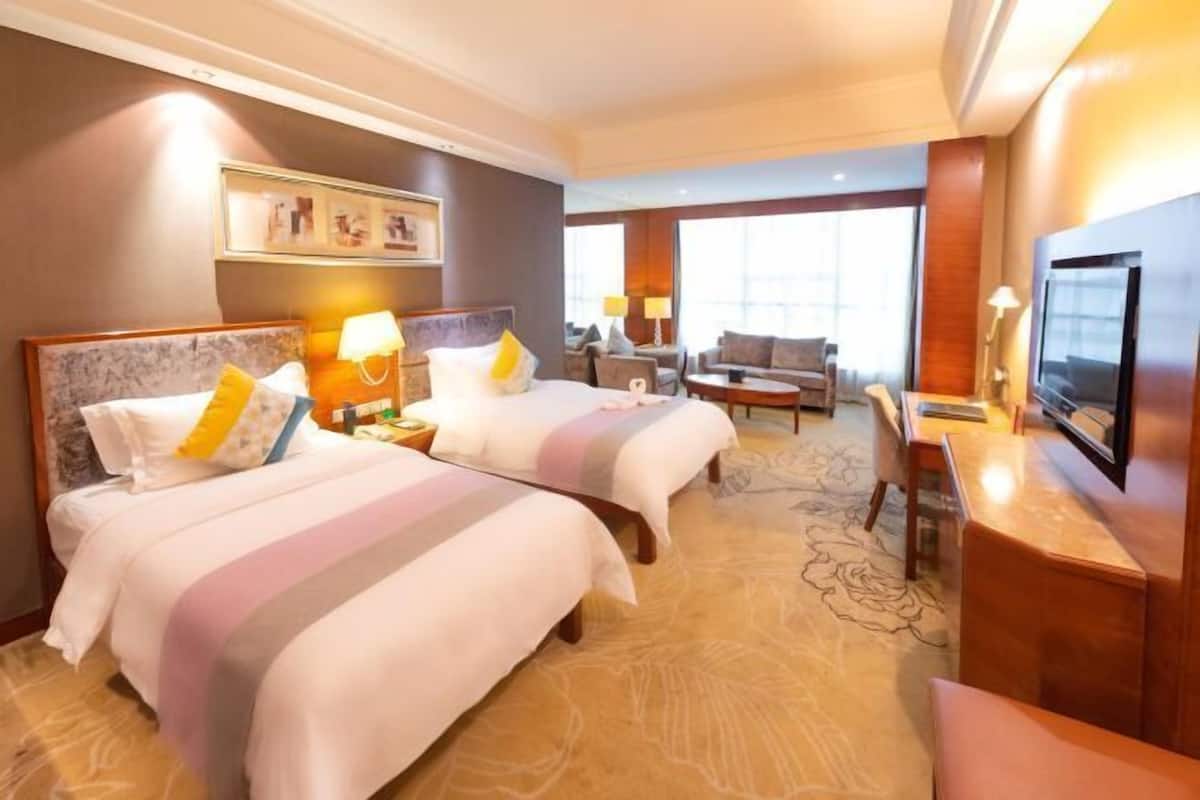 Habitación de hotel con dos camas, un escritorio, un televisor y un ventanal grande.