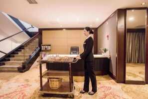 A hotel reception area with a reception desk, a trash bin, and a staircase. - Shenlong New World Hotel (Leiyang)