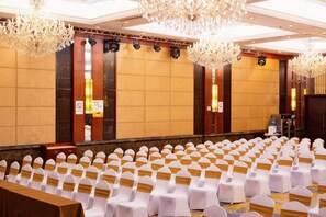 A conference room with rows of white chairs, a stage, and chandeliers.