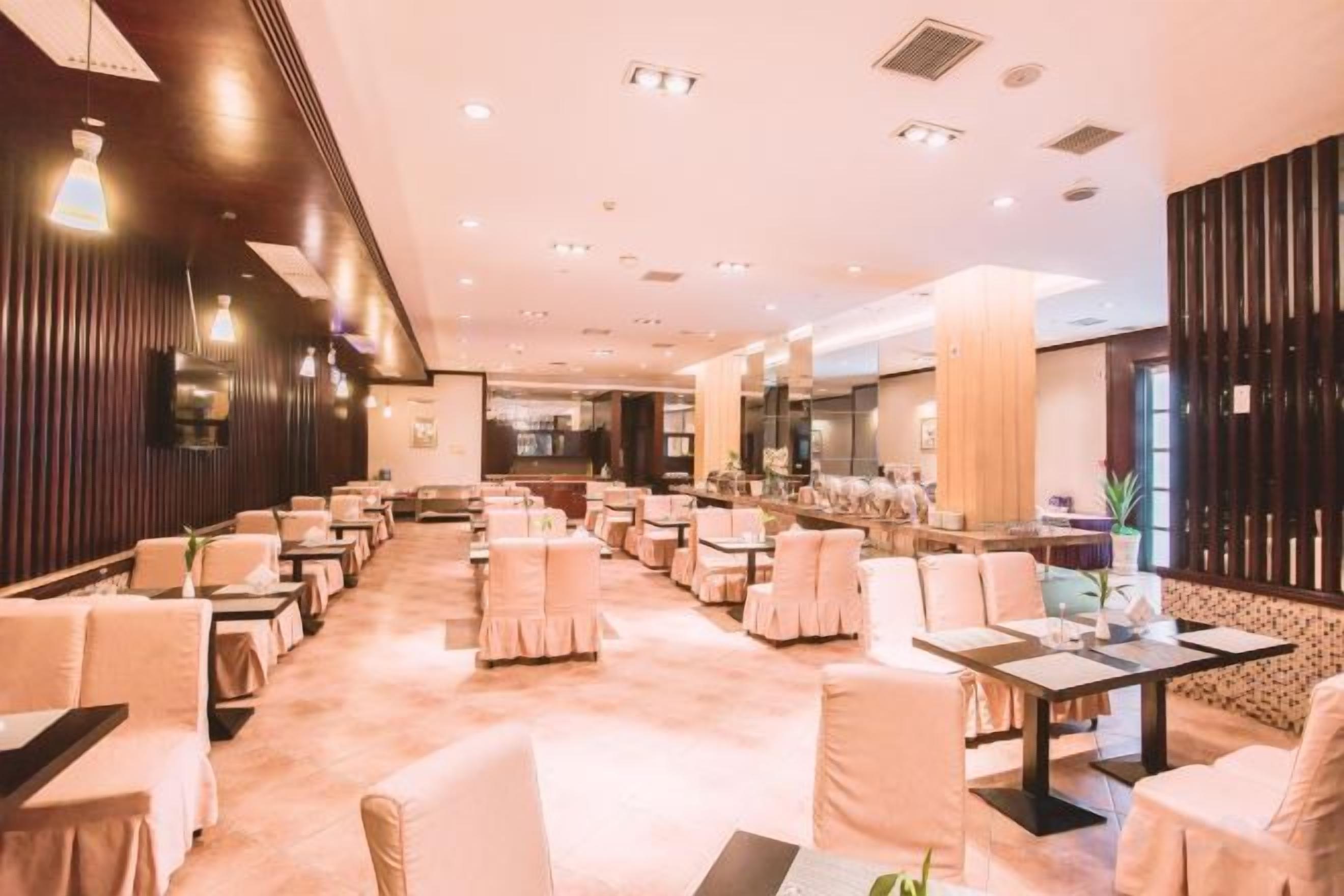 A hotel lobby with multiple seating areas, including tables and chairs, and a reception desk.