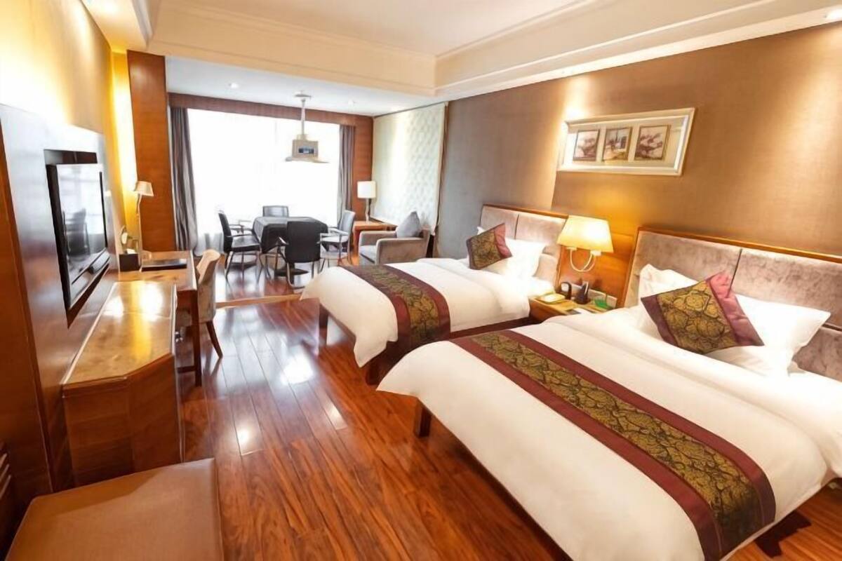 Habitación de hotel con dos camas, un escritorio, una televisión y vistas al exterior.