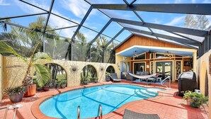 Ein Swimmingpool mit Glaskonstruktion, umgeben von Liegestühlen und Topfpflanzen.