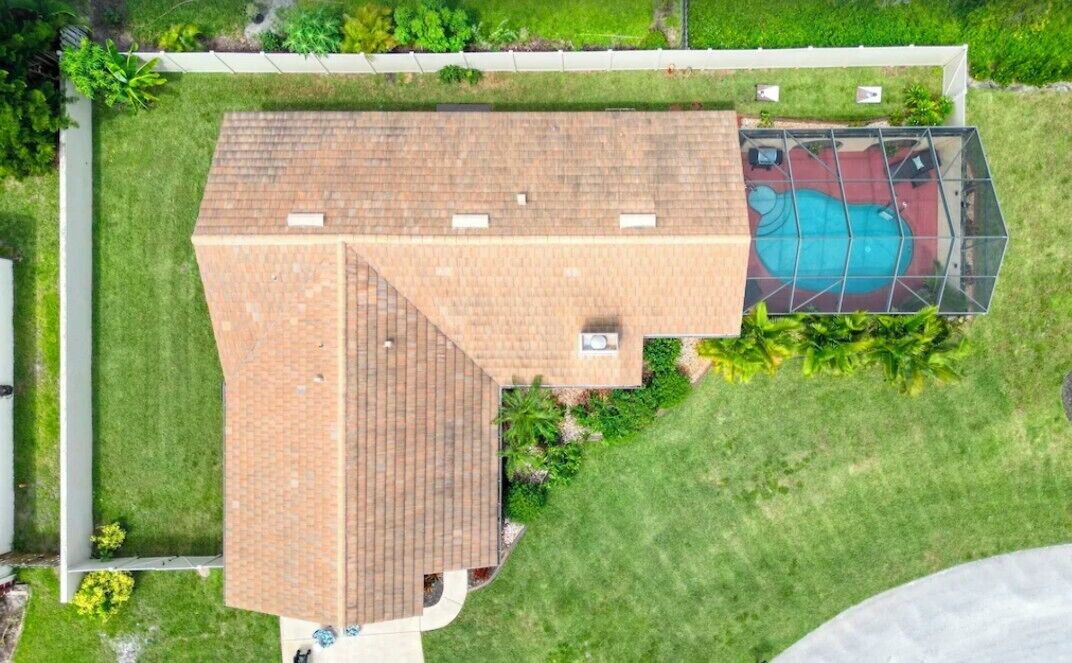 An aerial view of a house with a sloped roof, a swimming pool, and a well-maintained lawn.