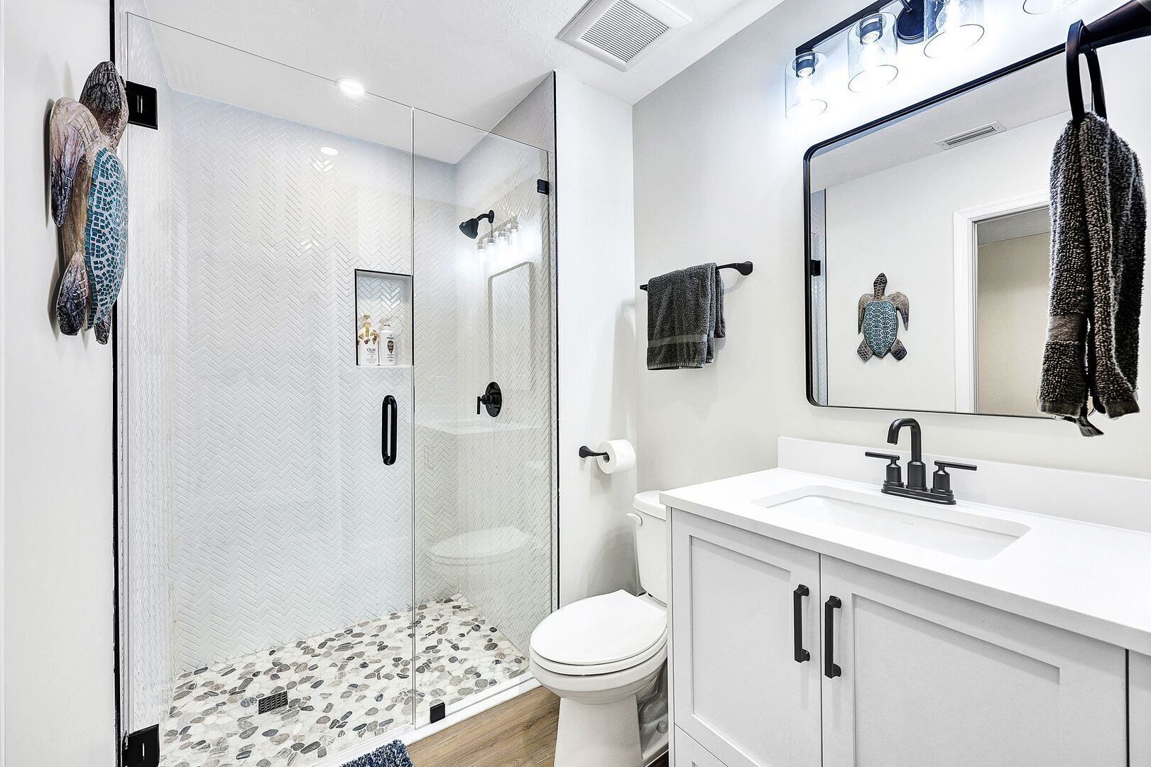 Un baño moderno con ducha de vidrio, lavamanos blanco y un espejo grande.