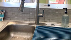 A kitchen with a stainless steel sink, a blue soap dispenser, and a window with a view of trees and a deck. - The Dogwood at Hamilton Cove ~ Peaceful Lakefront Cabin on Lake Hamilton (Royal)