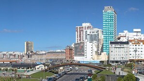A coastal cityscape with a prominent waterfront, a bridge, and a variety of buildings including a tall green-striped skyscraper. - Hotel Delfin (Mar del Plata)