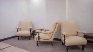 Three beige armchairs with wooden legs in a room with plain white walls and a tiled floor. - Hotel Delfin (Mar del Plata)