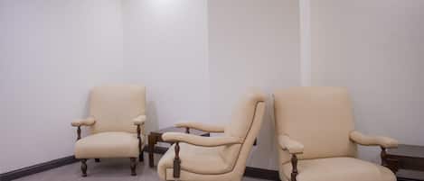Three beige armchairs with wooden legs in a room with plain white walls and a tiled floor.