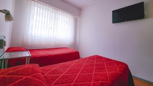 A room with two beds, a small table, a lamp, and a TV on the wall. - Hotel Delfin (Mar del Plata)