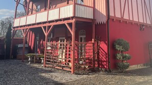 A red two-story building with a balcony and a covered porch area.