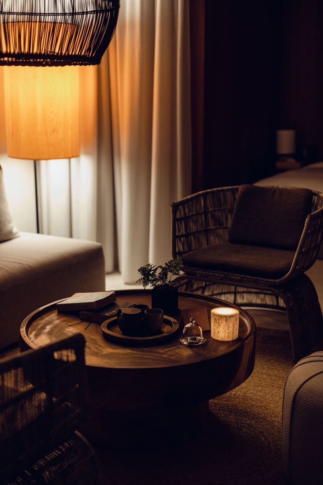 Una habitación acogedora con una mesa de centro de madera, una silla de mimbre, un sofá y una lámpara.