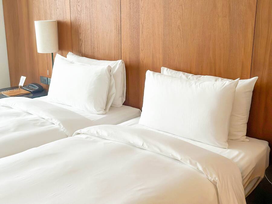A hotel room with a wooden headboard, two white beds, a bedside table with a lamp, and a phone.