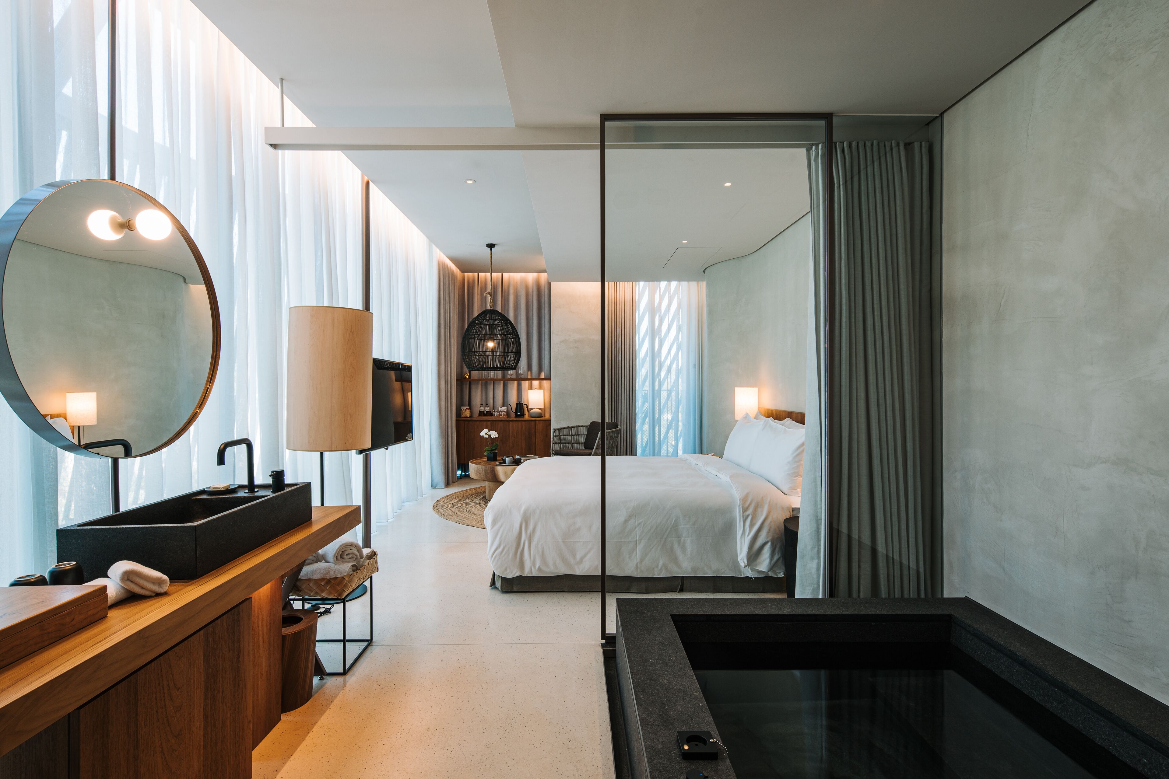 A modern hotel room with a large bed, a built-in sink, a mirror, and a bathtub.