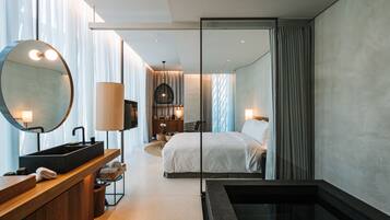 A modern hotel room with a large bed, a built-in sink, a mirror, and a bathtub.