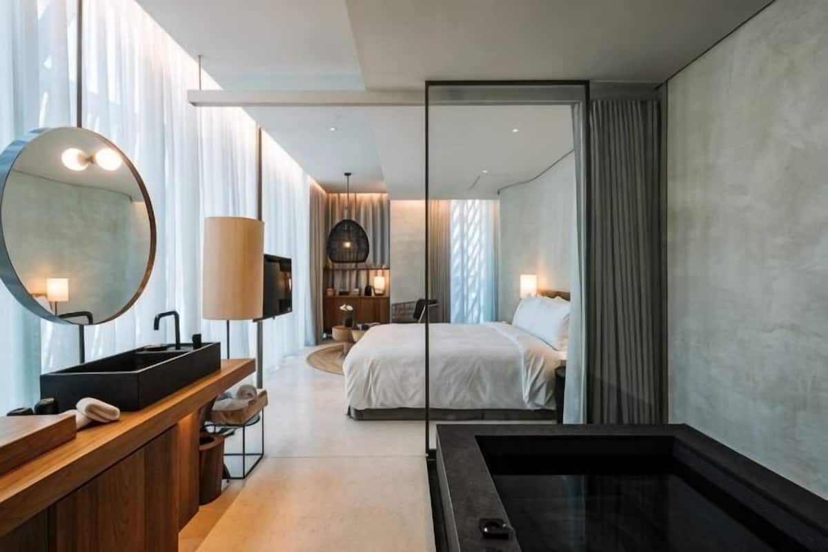 Une chambre d’hôtel moderne dotée d’un grand lit, d’une salle de bain séparée avec baignoire, d’une coiffeuse avec miroir et d’une vue accessible par une porte coulissante.