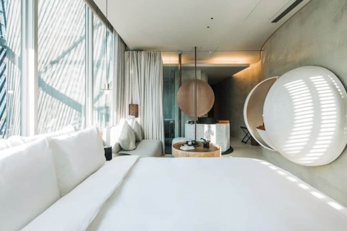 A modern hotel room with a large bed, a round table, and a seating area with a chair.