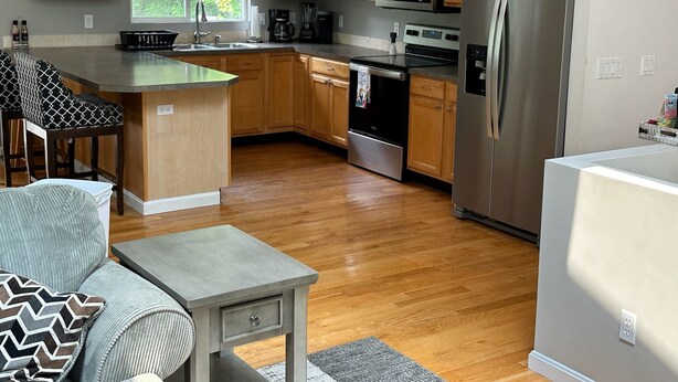 A modern kitchen with wooden cabinets, stainless steel appliances, a large window, and a bar area with stools. - Great Home in South County, Close to Narraganstt and Newport &.08 miles from URI (South Kingstown)