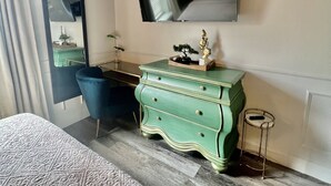 A hotel room with a bed, a desk, a dresser, a mirror, a television, and a small stool. - Historic Love, Modern Appeal C (Haines City)