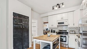 A modern kitchen with white cabinets, stainless steel appliances, and a chalkboard door with WiFi and emergency information. - Trendy Kensington | Espresso Maker| Garage| AC (Calgary)