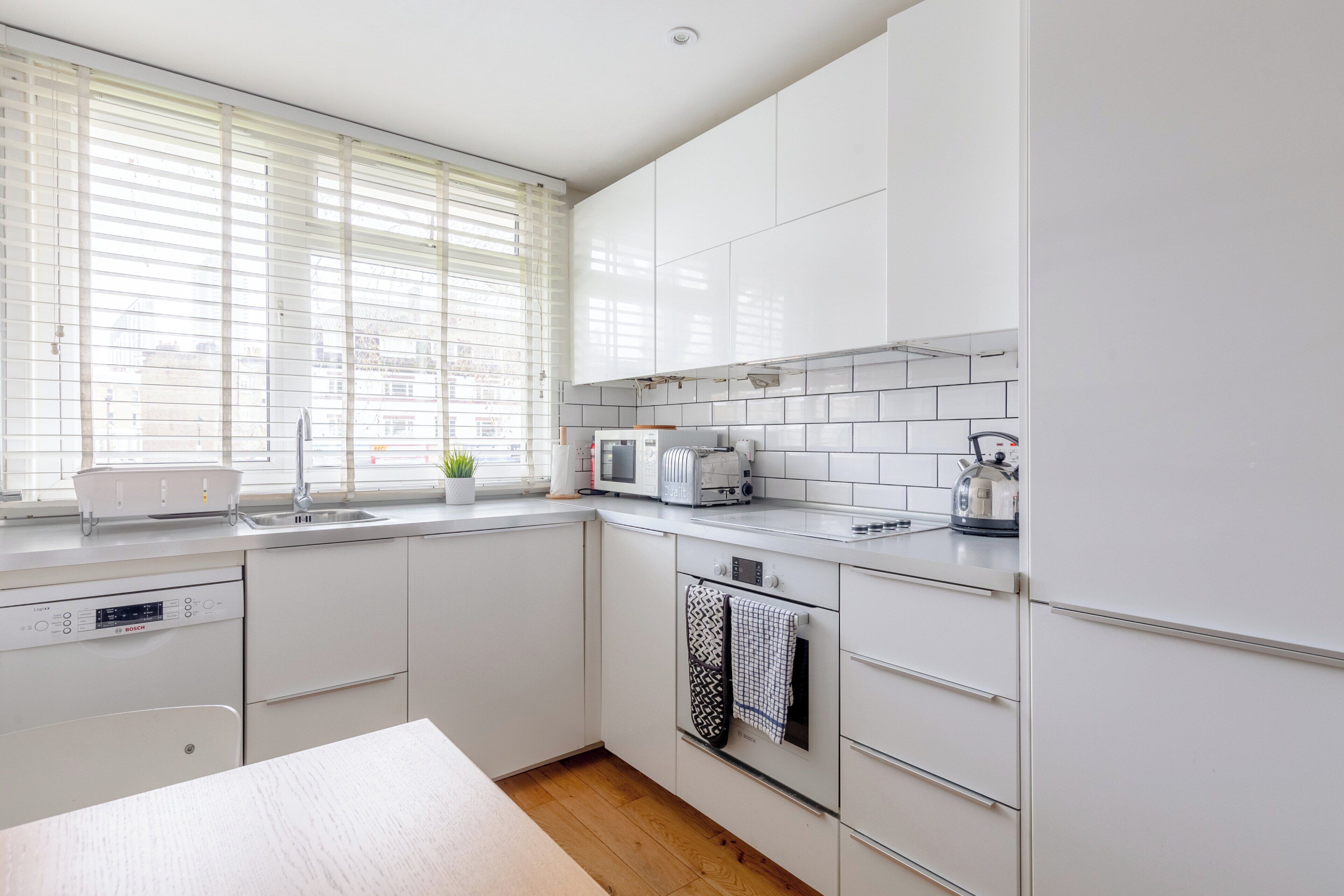Une cuisine moderne avec des meubles blancs, un lave-vaisselle Bosch, un four à micro-ondes et une bouilloire.