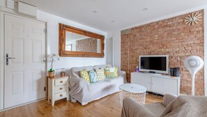 A modern living room with a brick wall, a television, a white cabinet, and a round table. - Peaceful Hidden Gem, Heart of South East London (London)