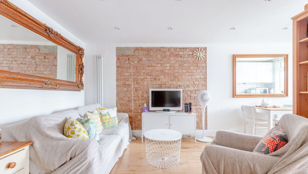 A modern living room with a brick wall, a television, a white round coffee table, and a comfortable seating area. - Peaceful Hidden Gem, Heart of South East London (London)