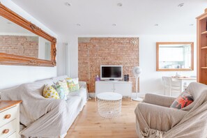A modern living room with a brick wall, a television, a white round coffee table, and a comfortable seating area. - Peaceful Hidden Gem, Heart of South East London (London)