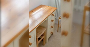 Un escritorio de madera con cajones y un estante, una silla y un radiador al fondo.