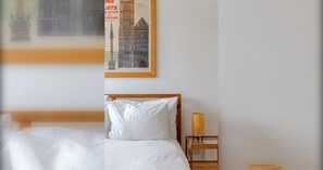 A hotel room with a bed, a nightstand with a lamp, and a framed picture of a building.