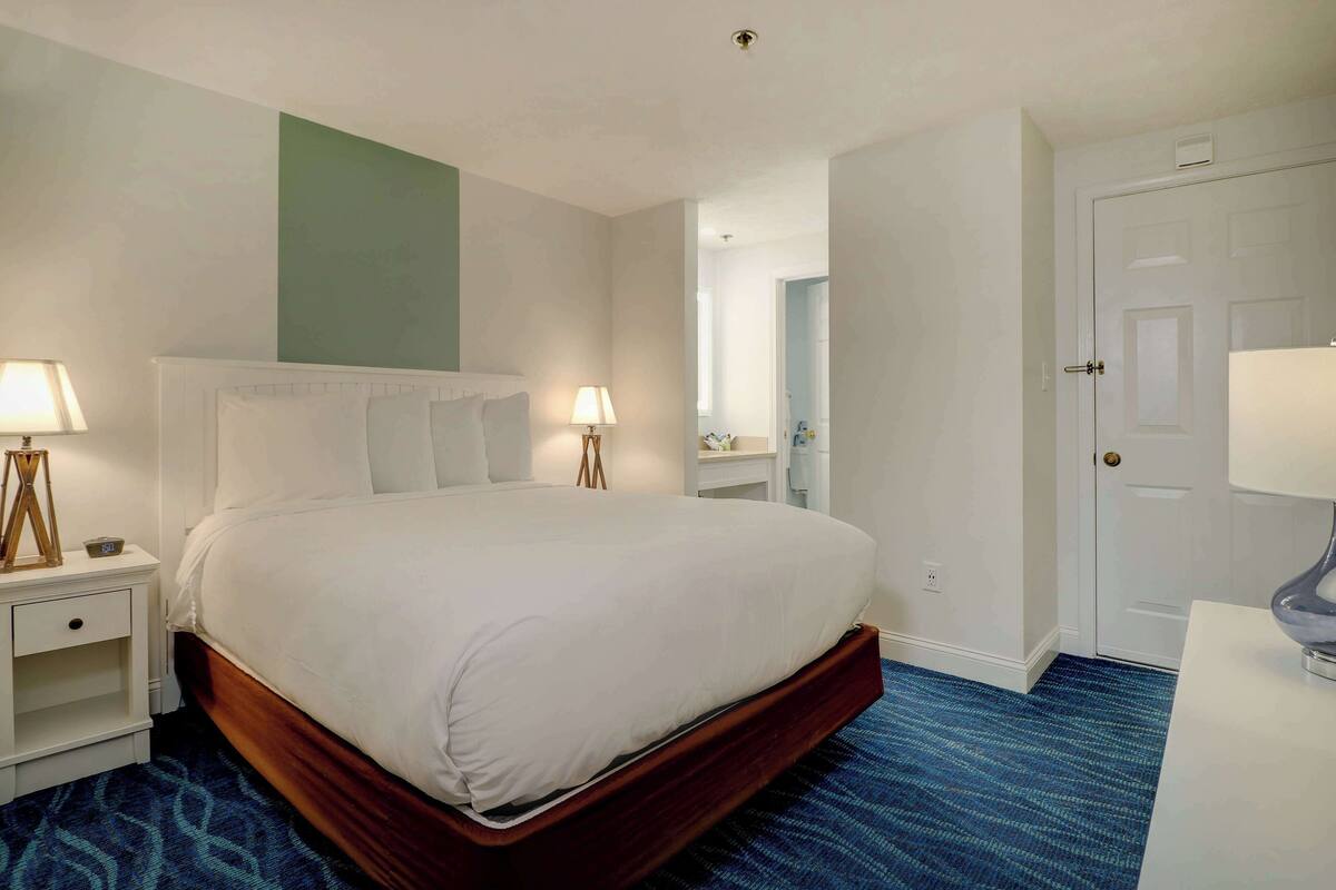 A hotel room with a large bed, bedside lamps, a dresser, and a door.