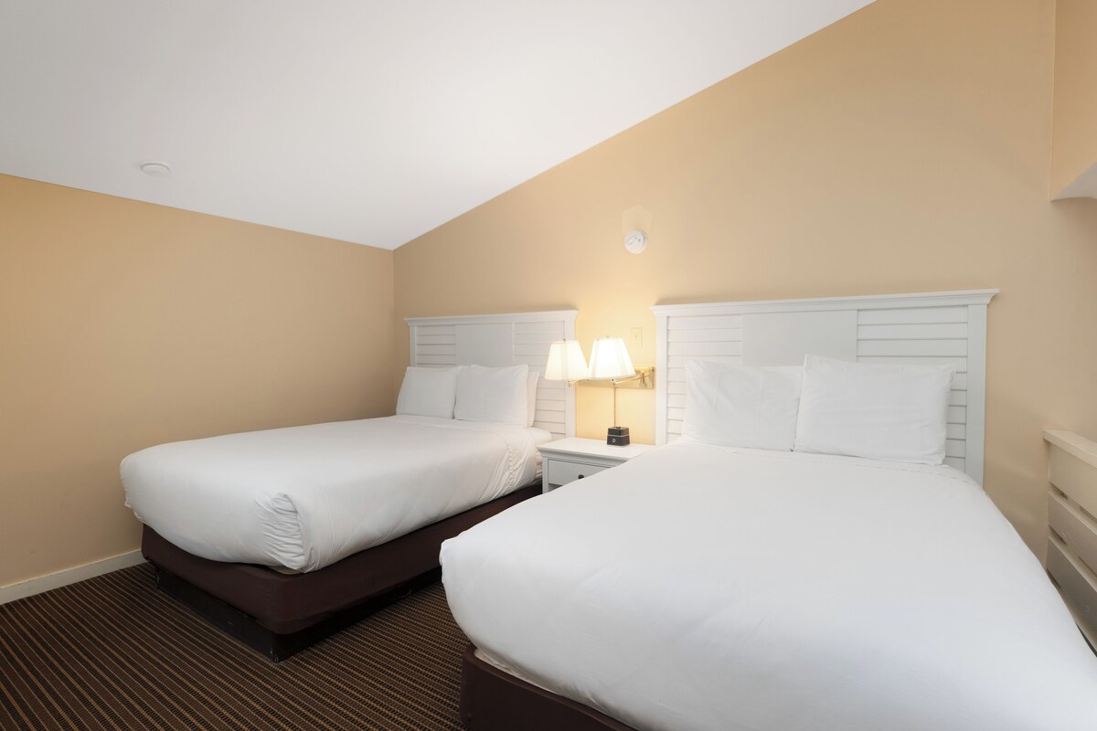 A hotel room with two single beds, a nightstand with a lamp, and a ceiling light.
