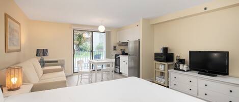 A modern hotel room with a large bed, a dining area, kitchenette, and a TV.