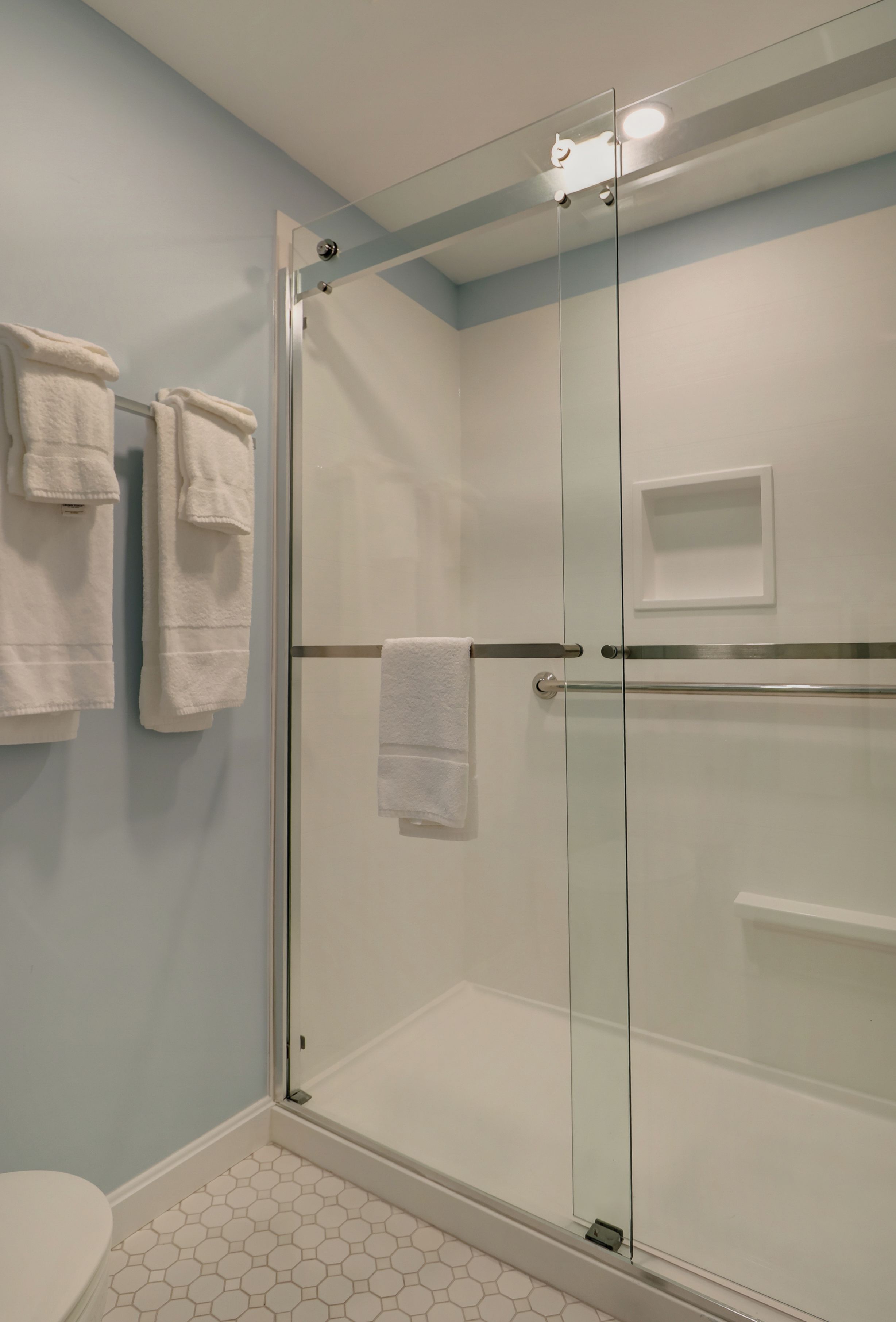 Un baño moderno con cabina de ducha de vidrio, inodoro y toallero con varias toallas.