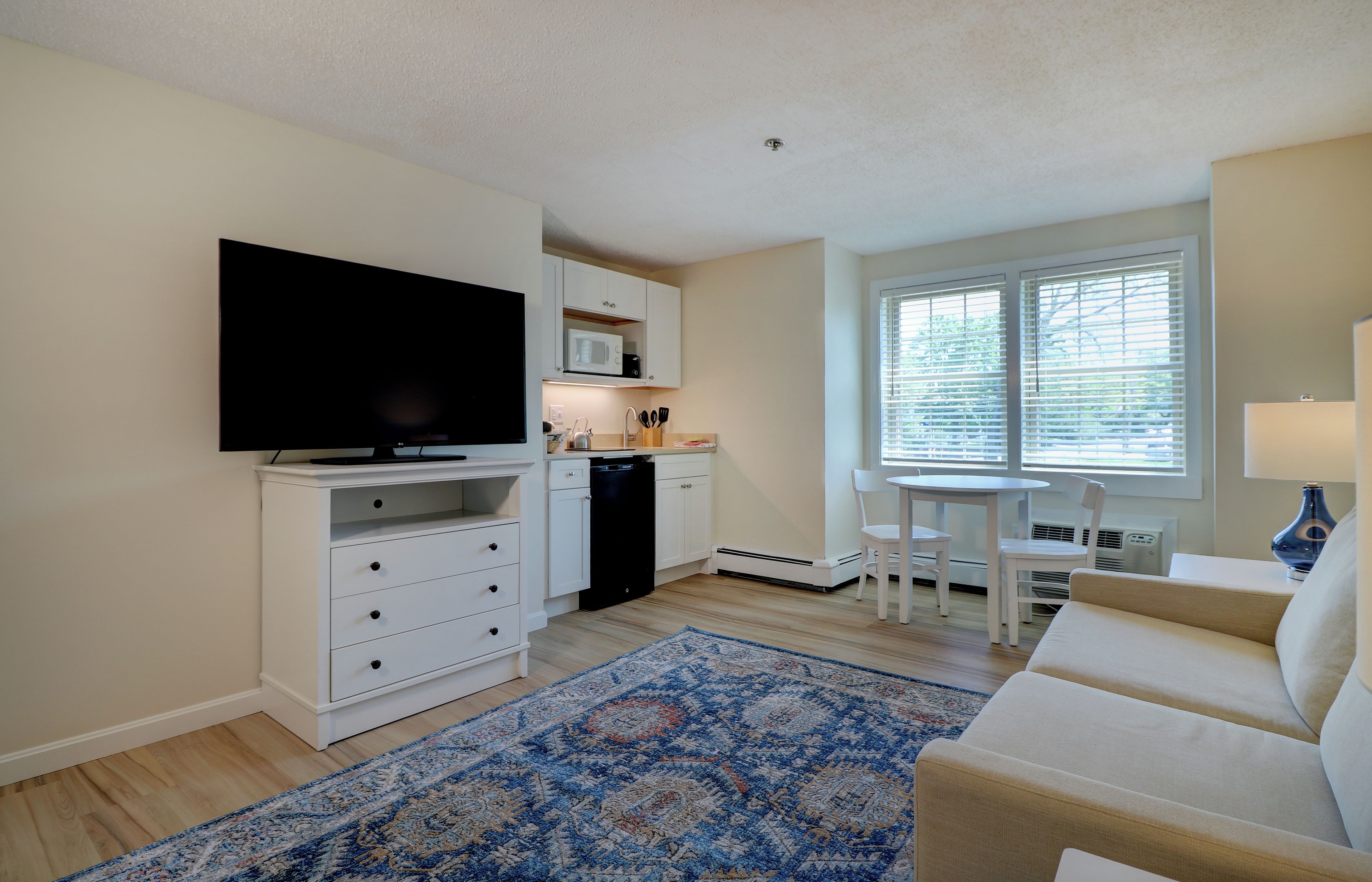 A compact living space with a flat-screen TV, kitchenette, dining area, and a patterned rug.