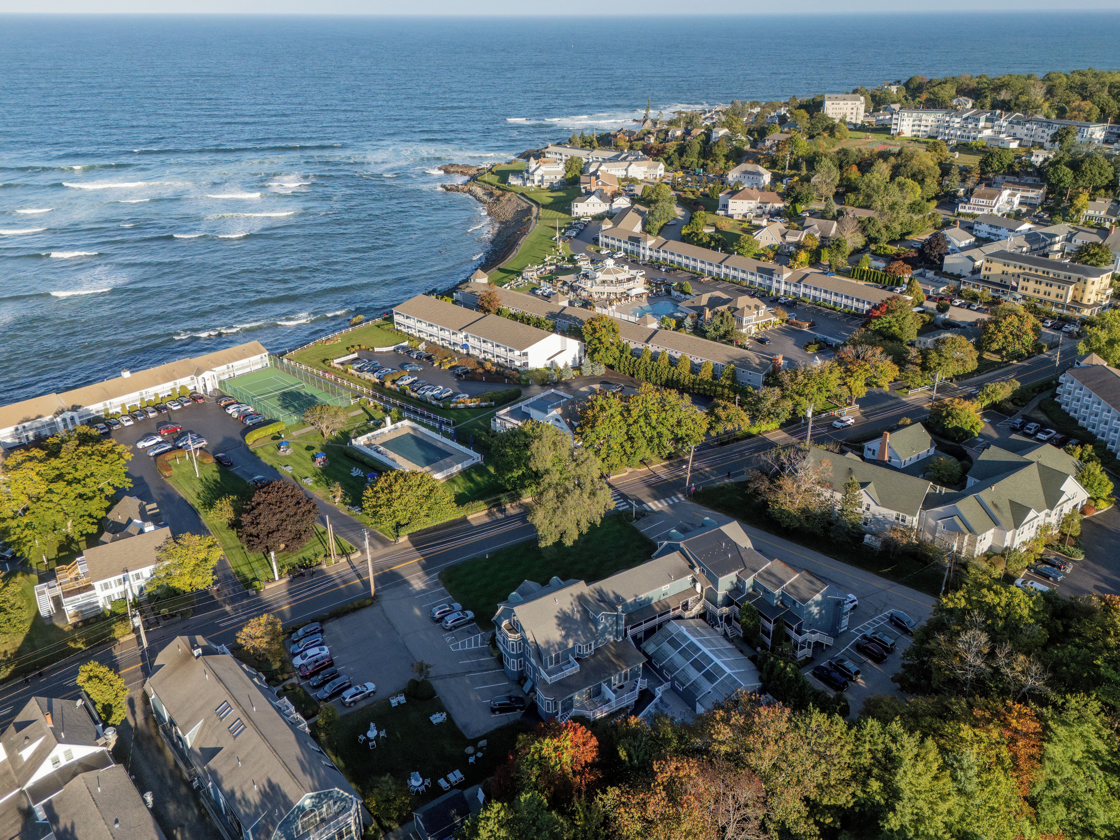 An aerial view of a coastal residential area with houses, a beach, and a large building with a parking lot.