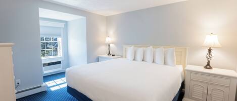 Une chambre d’hôtel avec un grand lit, deux tables de chevet avec des lampes, une fenêtre avec des stores et une moquette bleue.