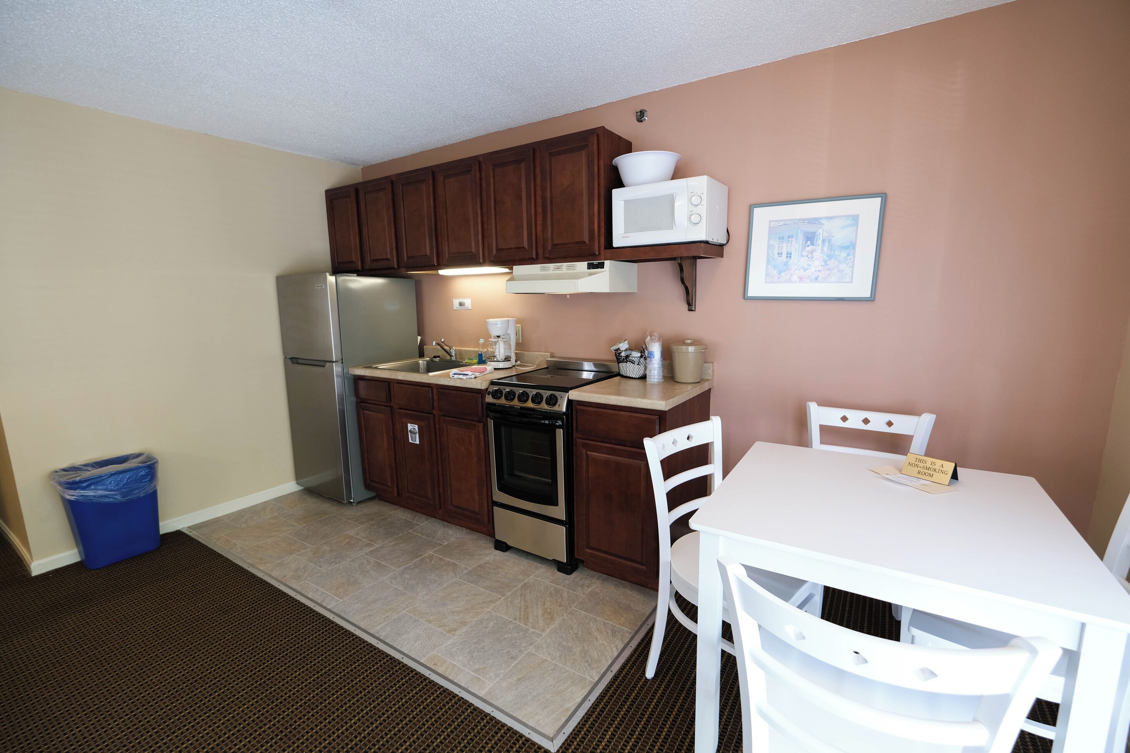 A compact kitchen with wooden cabinets, a stainless steel refrigerator, an oven, a microwave, and a small dining table with chairs.