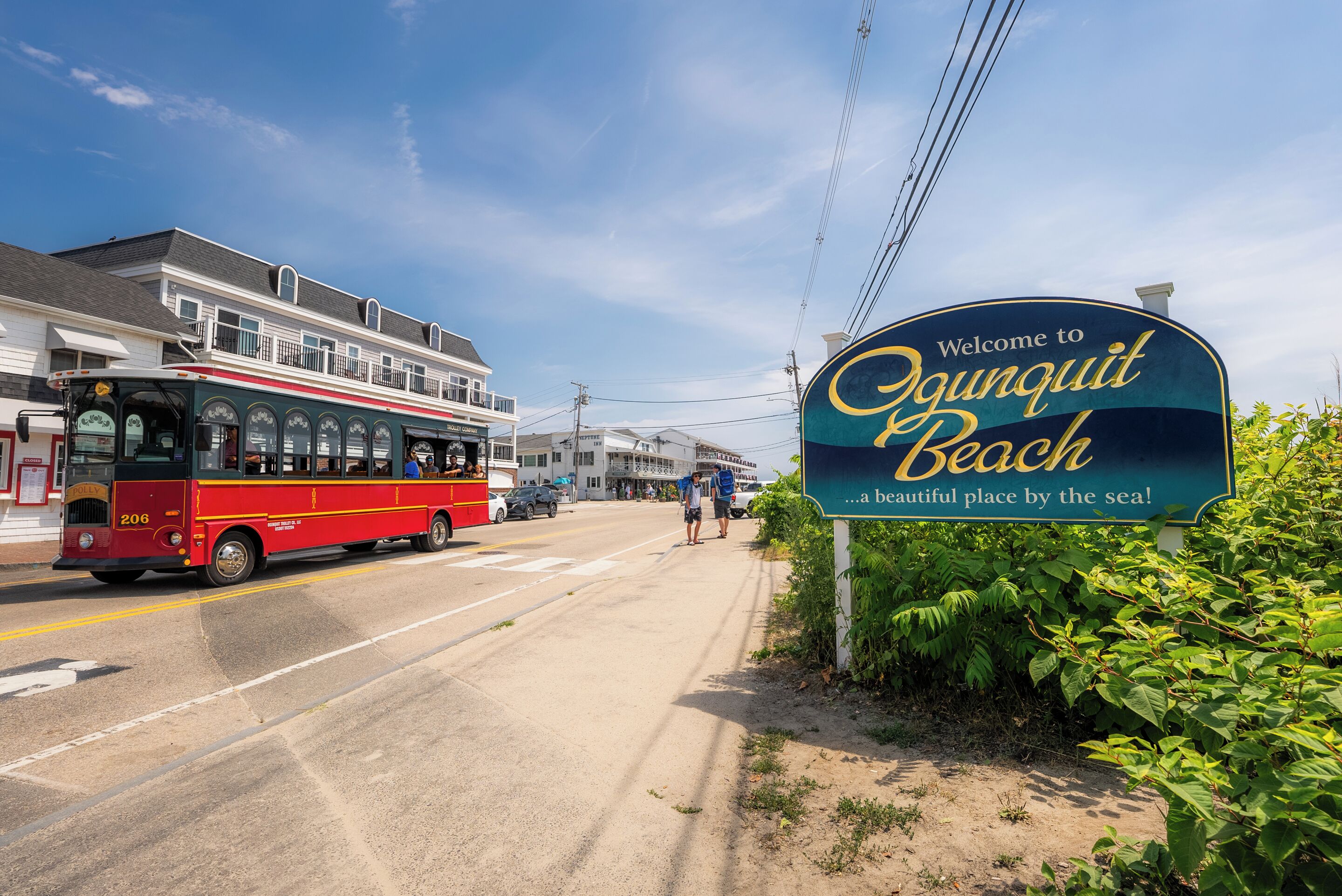 A street with a red bus and a sign welcoming to Ogunquit Beach.