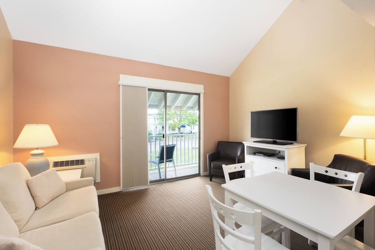 A hotel room with a sofa, a dining table, a TV, and a balcony with a view.