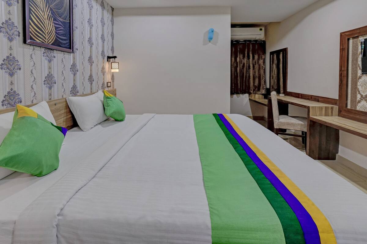 Quarto de hotel com uma cama bem arrumada, uma mesa de trabalho e uma cadeira.