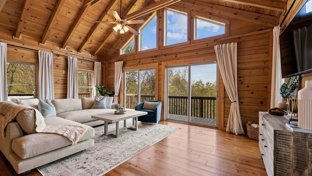 A spacious living room with a wooden ceiling, large windows, a sofa, a coffee table, and a TV. - Pisgah Paradise • Private • Game Room • Large Deck (Pisgah Forest)