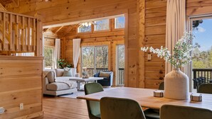 A wooden cabin interior with a dining area, sofas, and large windows. - Pisgah Paradise • Private • Game Room • Large Deck (Pisgah Forest)