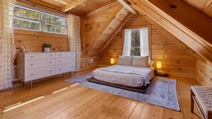 A cozy wooden bedroom with a bed, dresser, and two bedside lamps. - Pisgah Paradise • Private • Game Room • Large Deck (Pisgah Forest)