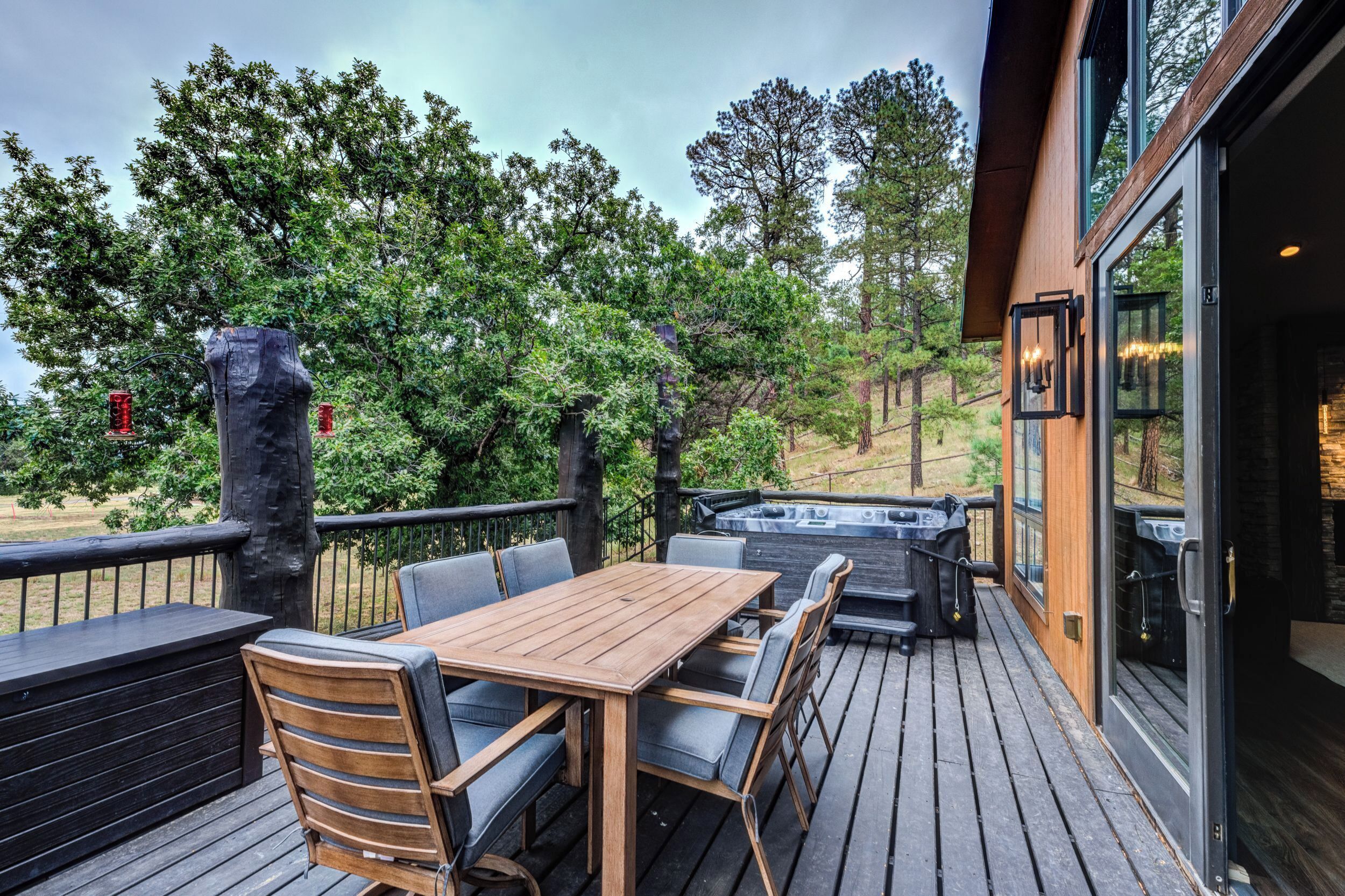 Een houten terras met een tafel, stoelen, een jacuzzi en uitzicht op bomen.