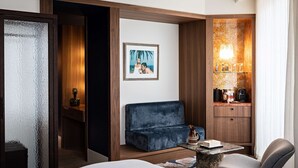 A hotel room with a bed, a blue sofa, a small table with a vase, a chair, a picture on the wall, and a minibar with bottles and glasses. - Hôtel Florida Paris (Paris)